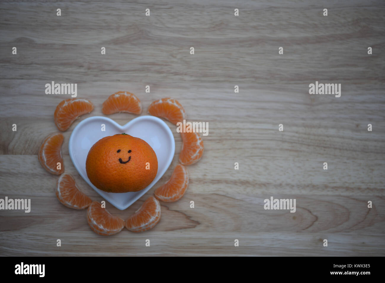Essen Fotografie eines gesunden orange Satsuma oder Tangerine oder Clementine mit auf Lächeln und Obst Segmente mit einem weißen Liebe Herzform Teller Stockfoto