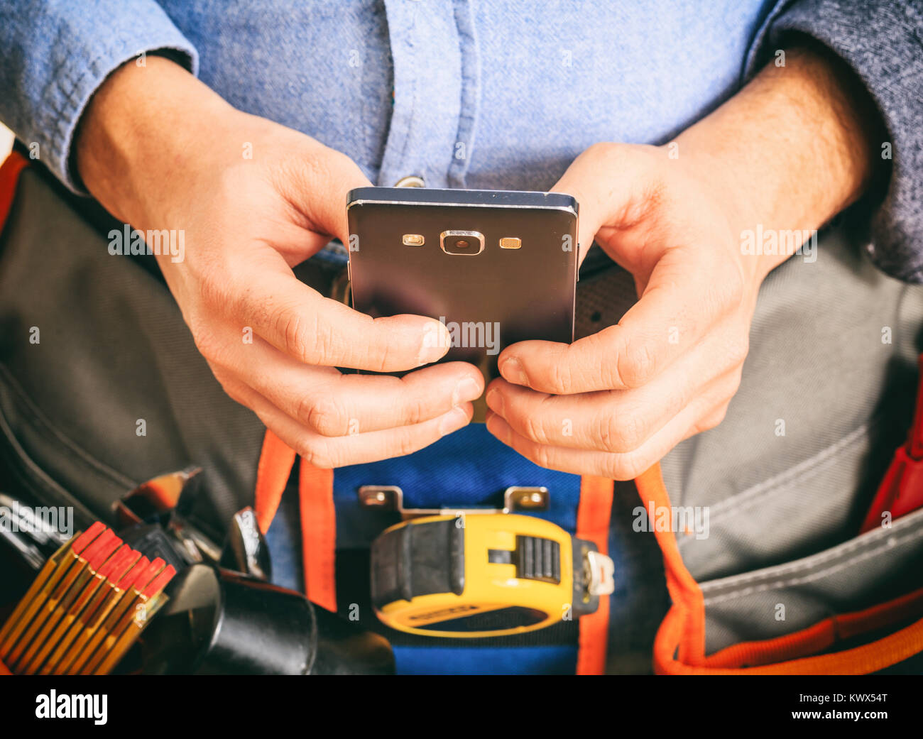 Arbeitnehmer mit einem Werkzeug Gürtel Holding ein Smartphone Stockfoto