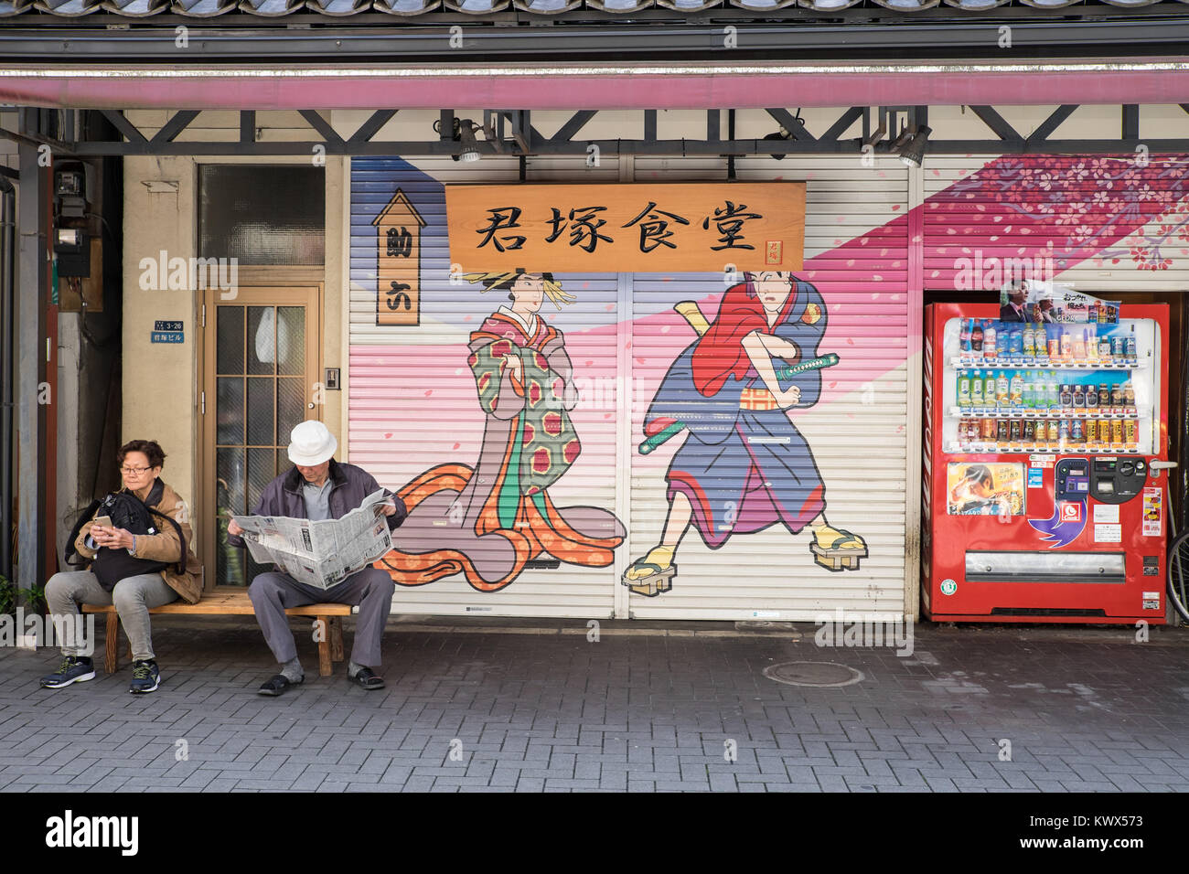 Japan, Tokio: zwei ältere Personen vor der Fensterläden aus Metall von einem Restaurant auf dem Kabuki Zeichen gezeichnet werden, Asakusa Viertel. Mann lesen Stockfoto