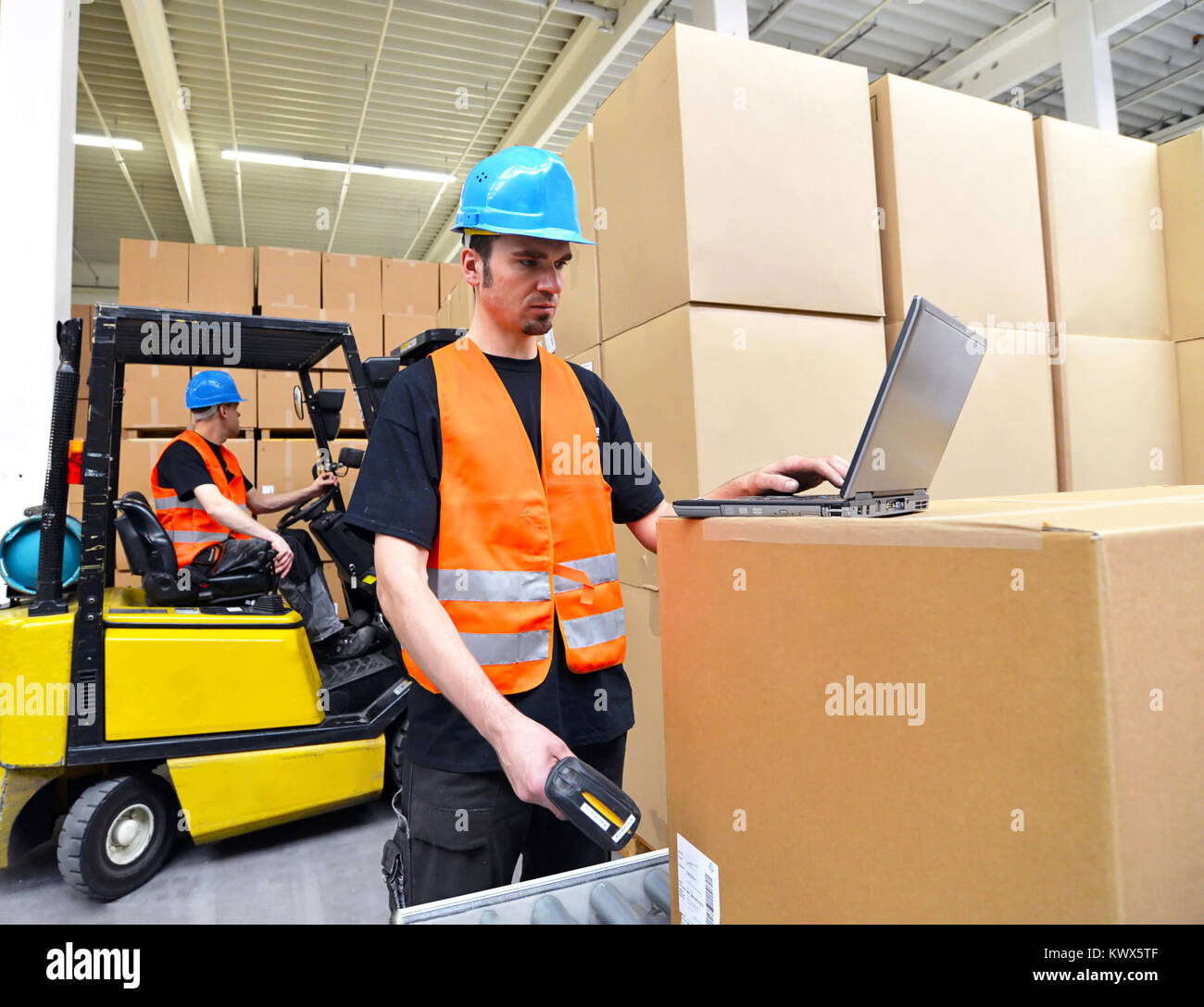 Arbeiter mit Notebook und Barcode Scanner verarbeitet eine Sendung im Kaufhaus - Gabelstaplerfahrer im Hintergrund Stockfoto