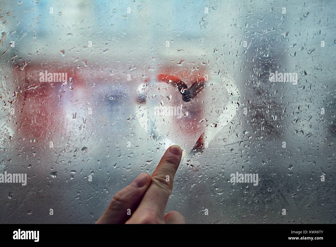 Finger des jungen Mannes Zeichnung Herz Form auf das Fenster mit Regentropfen gegen die Straße der Stadt. Stockfoto