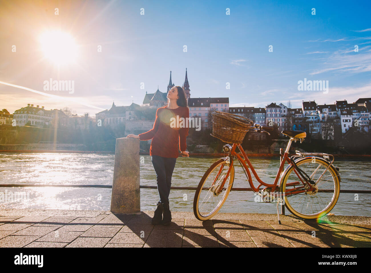 Ein schönes junges Mädchen steht auf dem Bahndamm in der Nähe einer Stadt  Fahrrad mit einem roten Korb in der Schweiz hat die Stadt Basel weit  entfernt ist Dom und Alte Hou