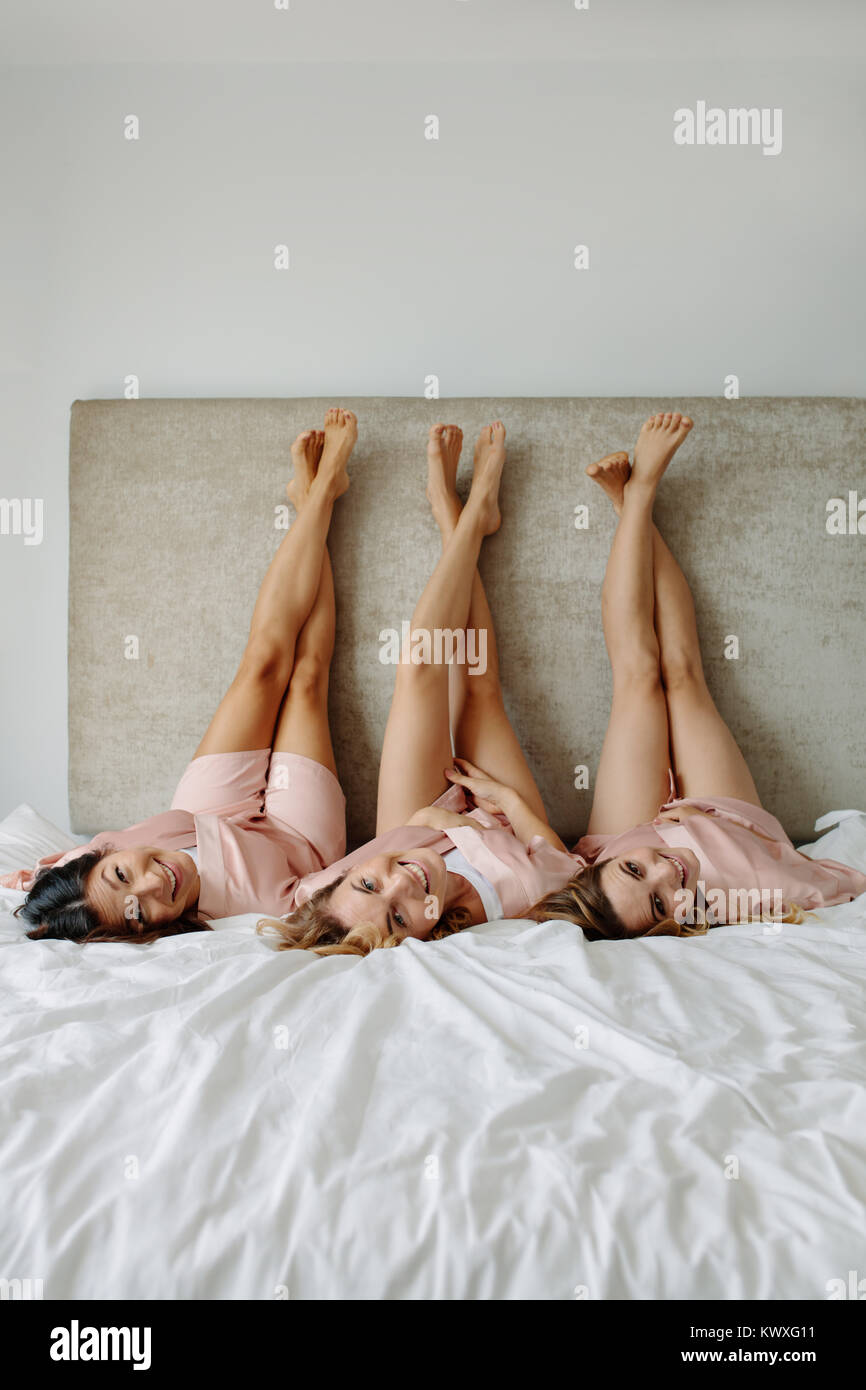 Junge Weibchen auf dem Bett mit den Beinen hoch und lächelte. Frauen in Schlafrock im Schlafzimmer liegen mit Beine angehoben. Stockfoto