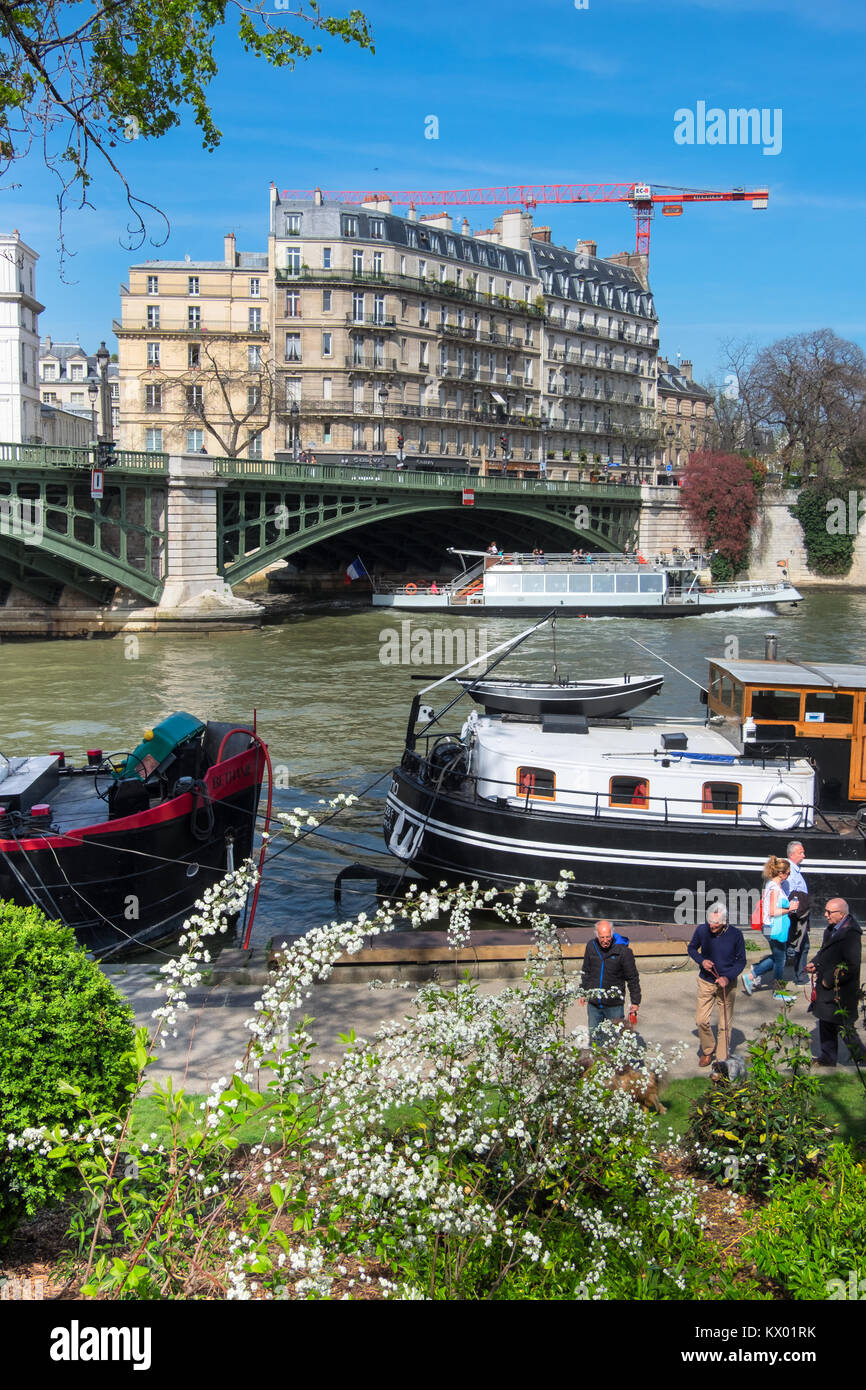 PARIS, Frankreich - 20 April 2016: Passagierschiffe pass Ile Saint-Louis, wie Leute Spaziergang entlang des Flusses durch die Gärten von Quai Saint Bernard. Stockfoto