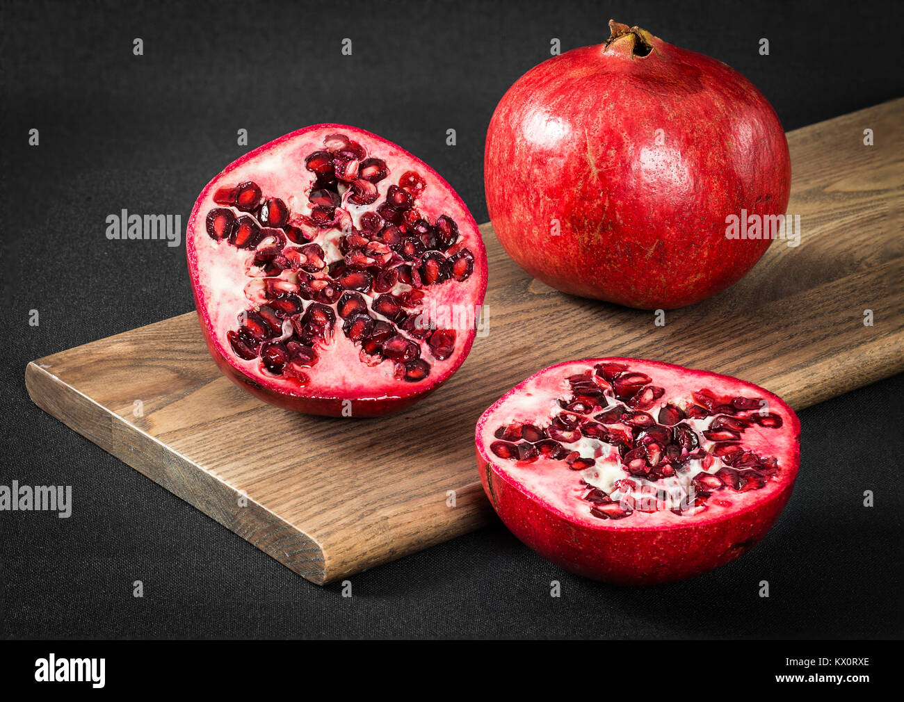 Eine geschnittene Granatapfel auf einem Schneidebrett mit einer ganzen Granatapfel. Schuß auf schwarzem Hintergrund Stockfoto
