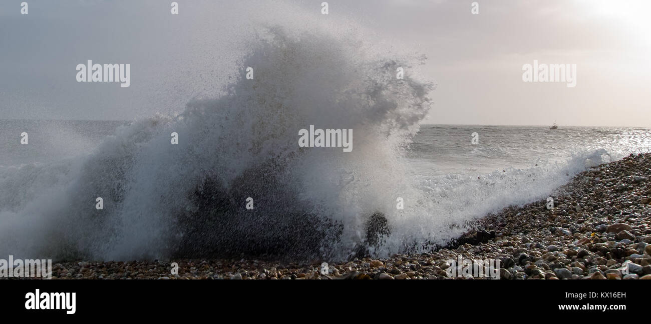 Storm wave schlagen Strand mit Fischerbooten in der Ferne in Selsey, West Sussex, Großbritannien Stockfoto