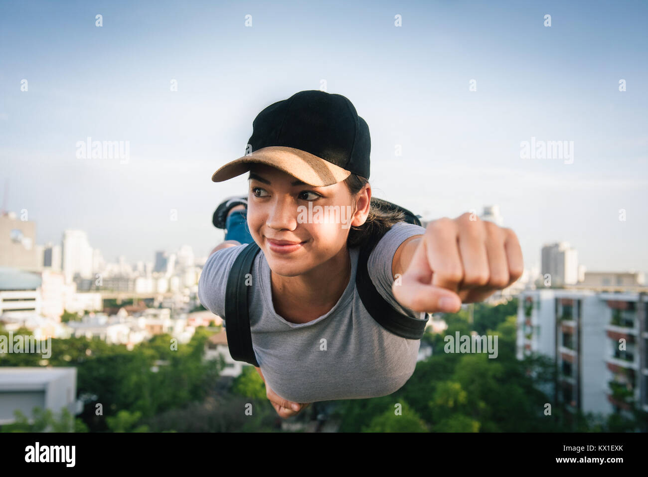 Eurasischen (halb europäisch, halb Asiatisch) Mädchen fliegt durch die Stadt Himmel wie superwoman trägt eine Kappe und einen Rucksack Stockfoto