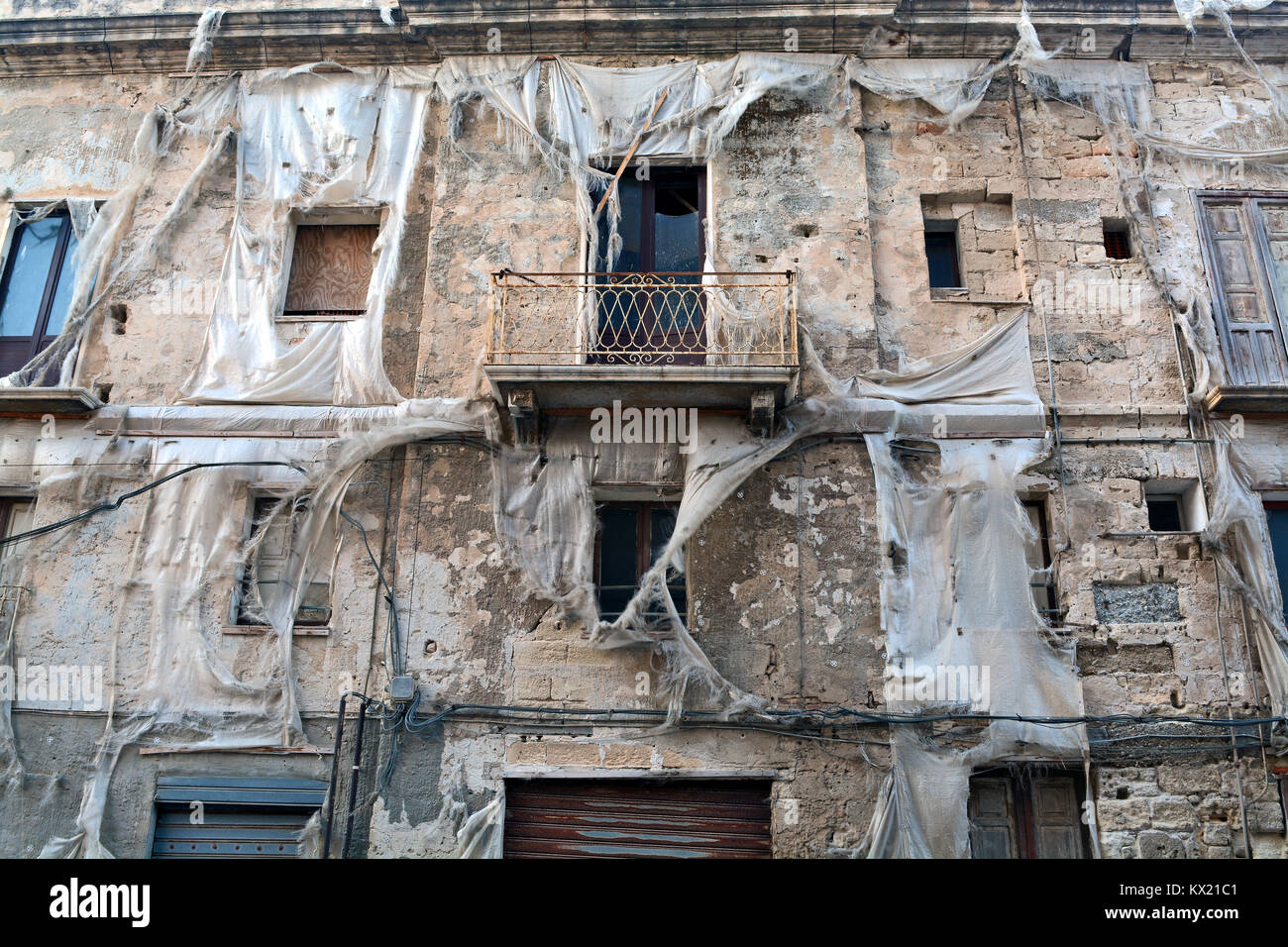 Detail der Fassade eines alten und baufälligen Gebäude in Trapani, Sizilien (Italien) mit Fetzen von kunststoffplanen über den Fenstern. Stockfoto