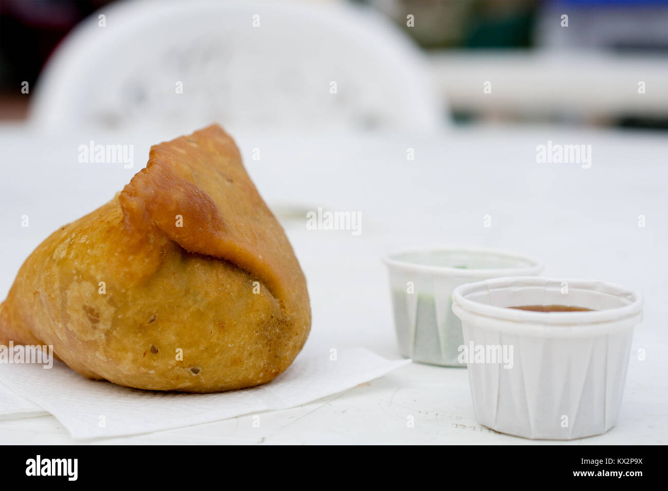 Ein ganzes Samosa auf Weiß Serviette mit indischen Gewürzen in durchführen, mini-cups auf weißem Kunststoff Tabelle eines Farmers Market, von der Seite viwed begleitet Stockfoto