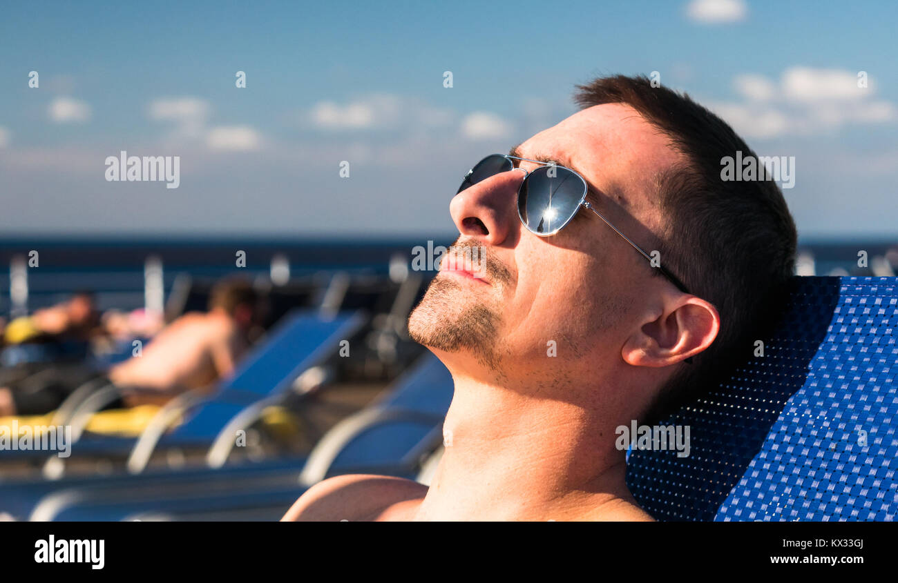 Porträt eines Mannes mit Sonnenbrille auf einem Strand Lounge Chair auf dem Deck eines Kreuzfahrtschiffes. Stockfoto