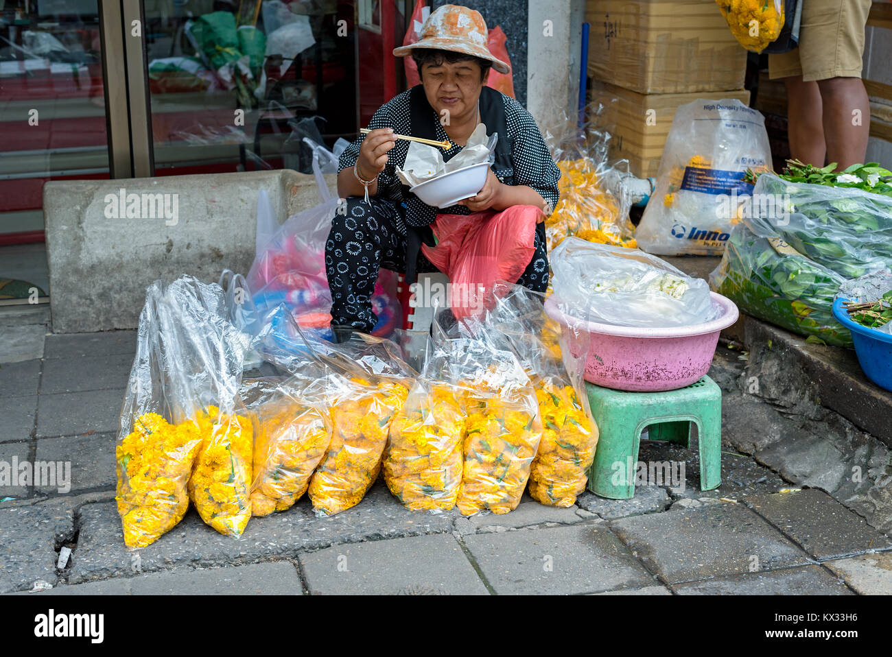 Ein Thai Street Hersteller nimmt ihre Mittagspause vom Verkaufen große Taschen von gelben Nelken auf einem Bangkok Seitenstraße. Stockfoto