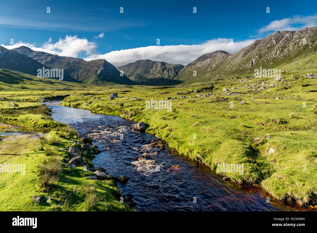 Connemara Landschaft in Irland: Ein Fluss fließt inmitten der Wiesen vor der majestätischen Berge Twelve Bens Stockfoto