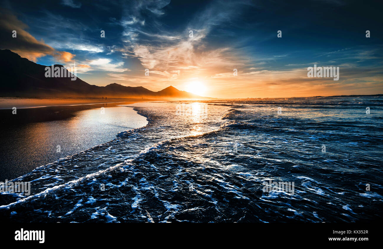 Strand Sonnenuntergang mit endlosen Horizont und einsame Figuren in der Ferne und unglaubliche schäumenden Wellen. Vulkanischen Hügel im Hintergrund Stockfoto