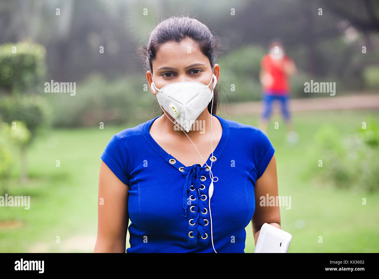 Junge Frau Umweltverschmutzung Hören von Musik Ohrhörer Garten Stockfoto