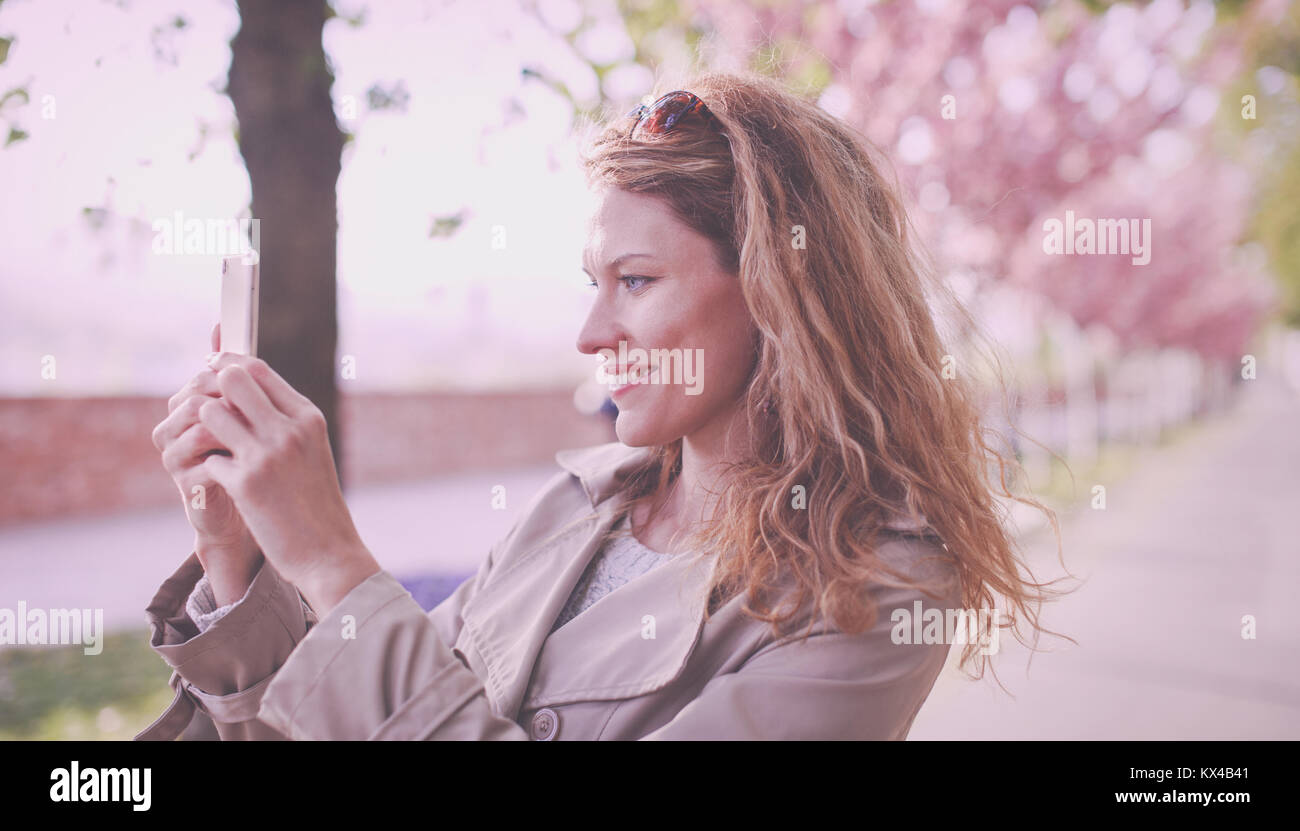 Junge natürliche Frau mit lockigem Haar schießen durch Smartphone in Park am Frühling Stockfoto