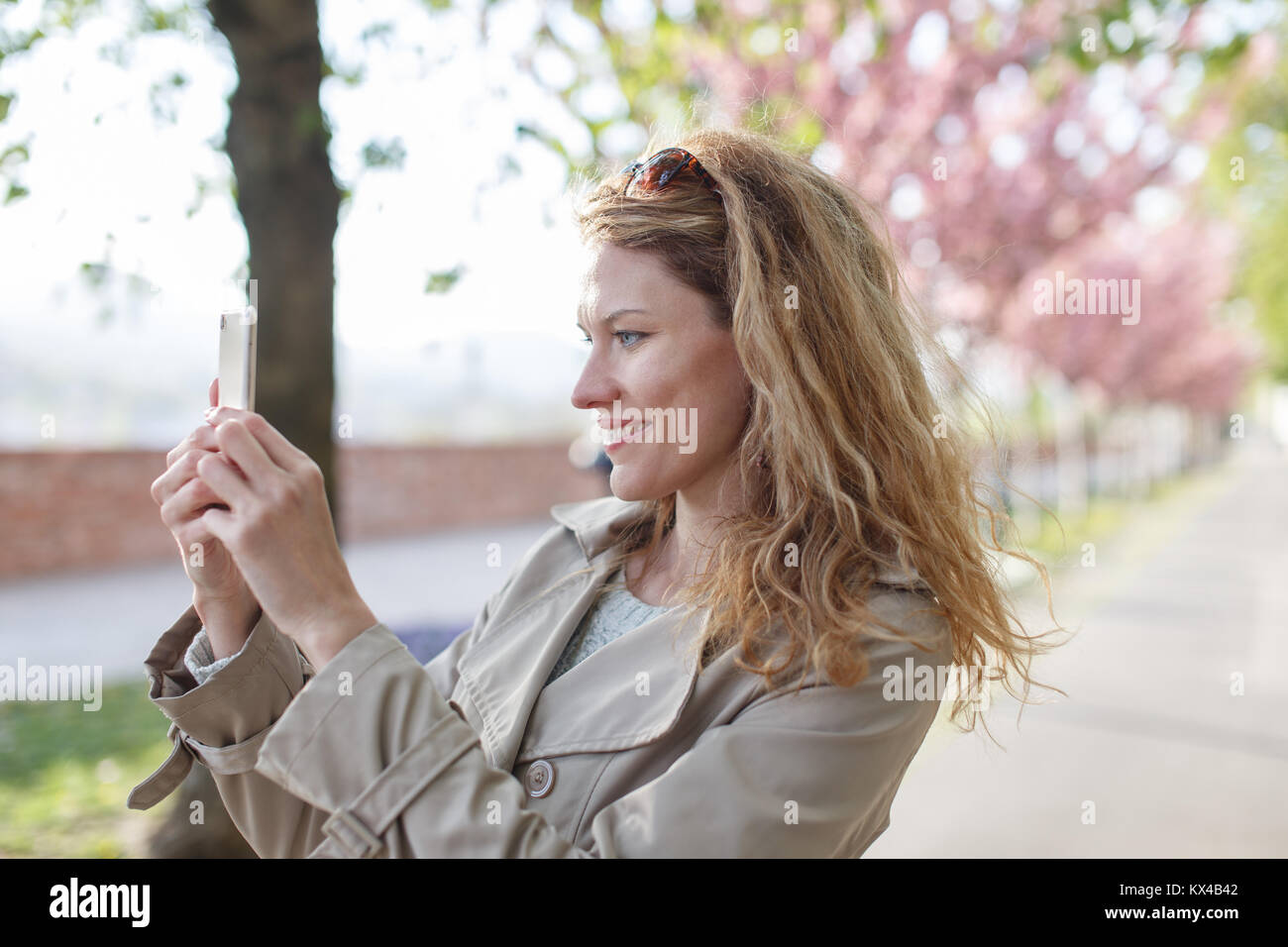 Junge natürliche Frau mit lockigem Haar schießen durch Smartphone in Park am Frühling Stockfoto