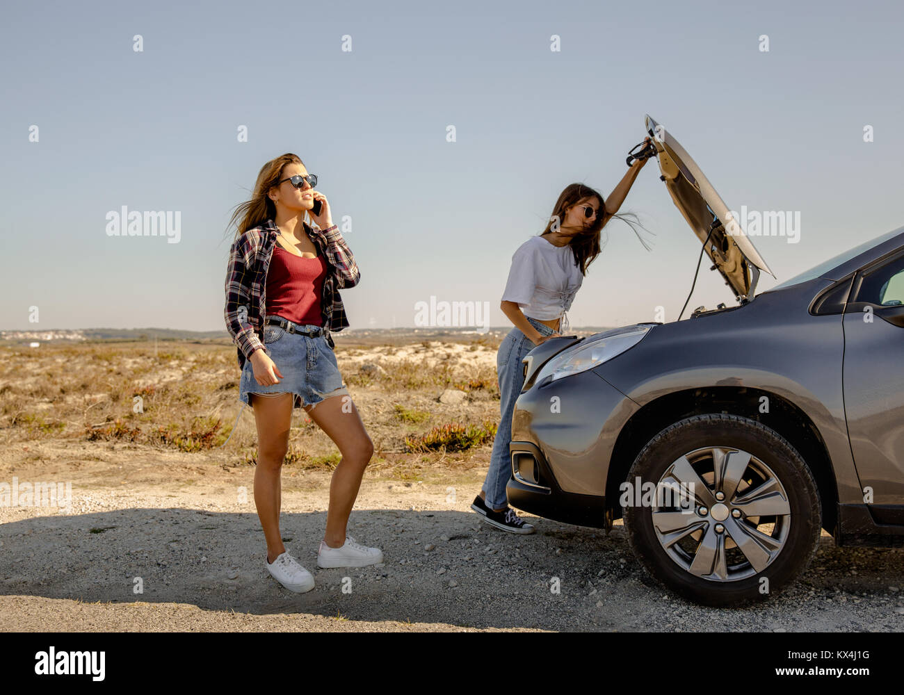Die Frau in der Nähe ein Auto mit Motorschaden und ihr Freund fordert Soforthilfe Stockfoto