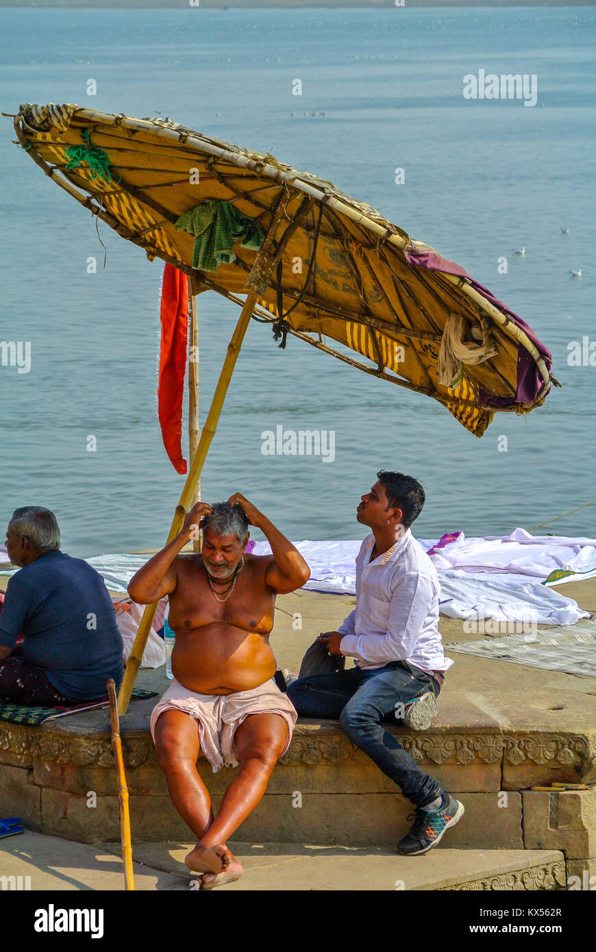 Ein indischer männlicher Pilger unter einem Sonnenschirm von einem Ganges, Varanasi, Indien Stockfoto