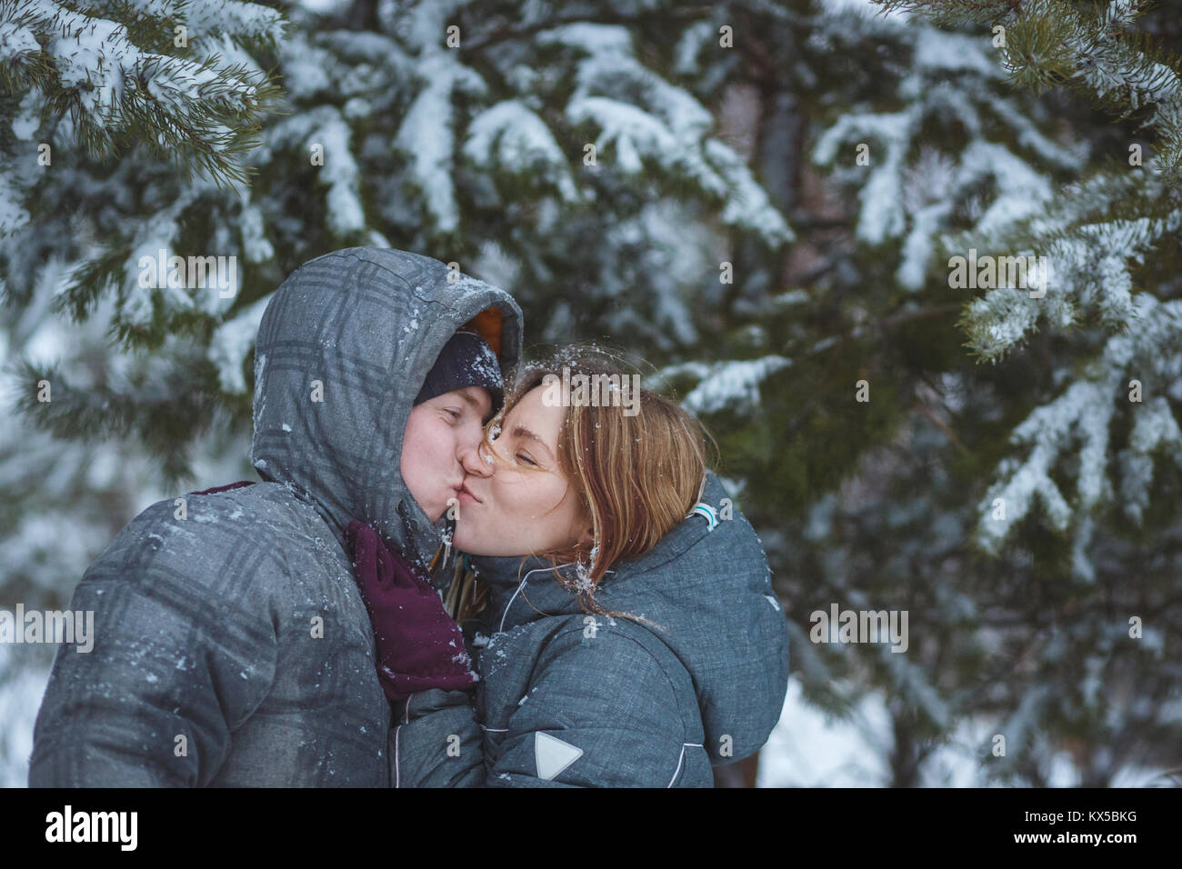 Gerne Schnee paar Küssen unter Tannenzweigen im Winter Wald. Konzept gesunde romantischen Urlaub an der frischen Luft Stockfoto
