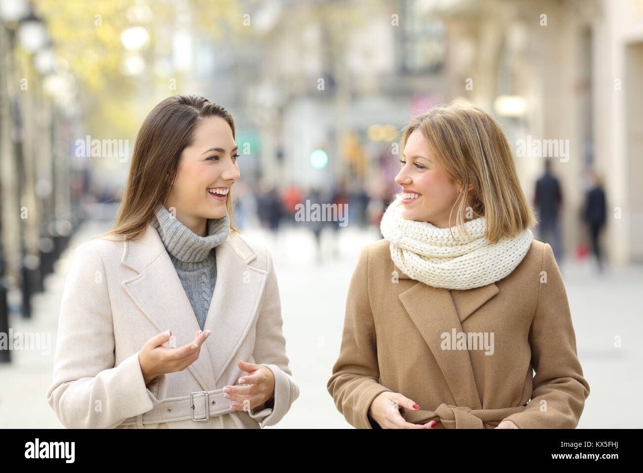 Vorderansicht Porträt zweier Frauen Freunde tragen Mäntel sprechen und gehen auf die Straße Stockfoto