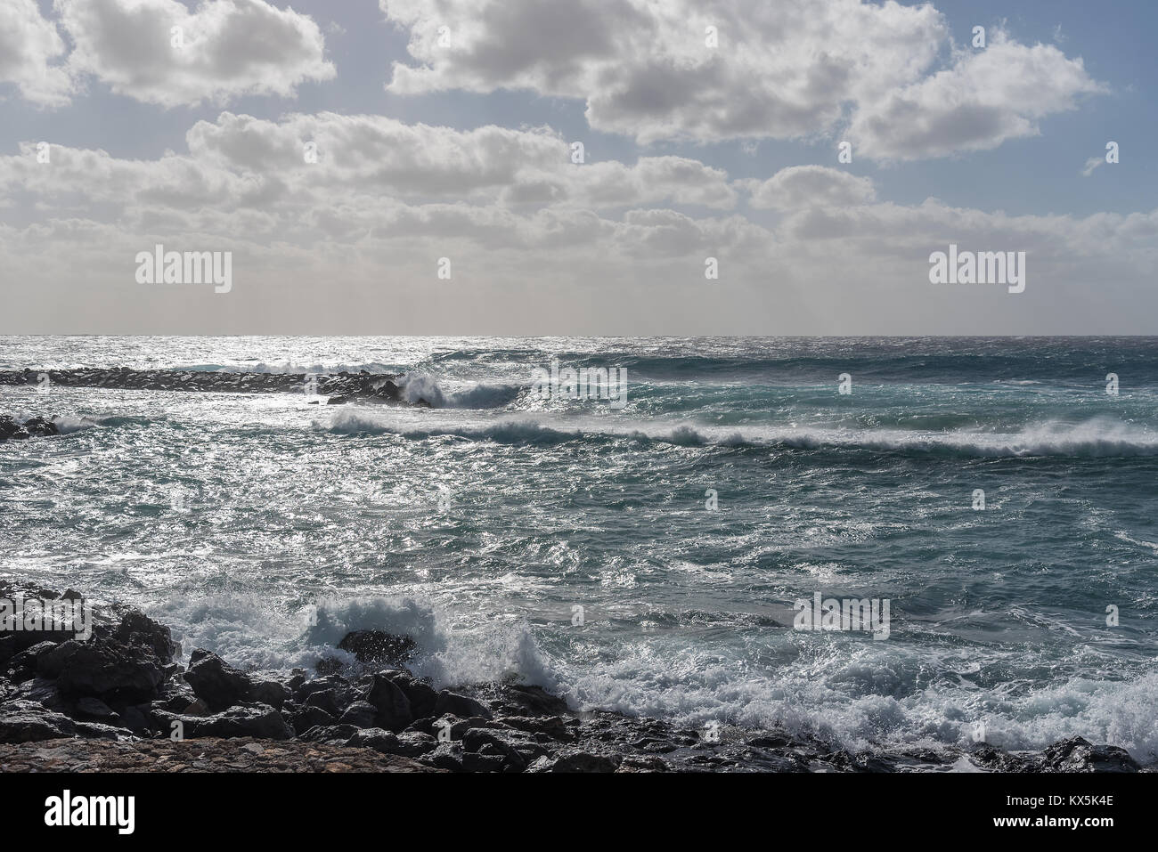 Ein sehr stürmischer Tag in Costa Teguise auf Lanzarote lässt Wellen am Strand brechen. Der Himmel ist wolkenverhangen und der Regen wird prasseln. Stockfoto