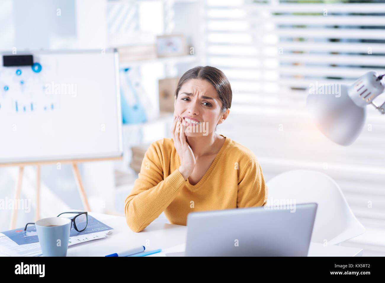 Emotionale Frau sitzt und Leiden von Zahnschmerzen bei der Arbeit Stockfoto