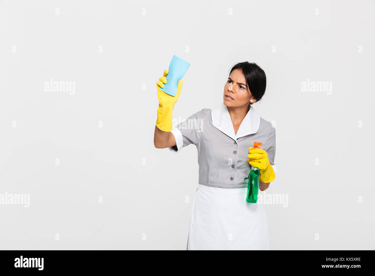 Junge konzentriert Mädchen in Uniform Reinigung Fenster mit der rag auf weißem Hintergrund Stockfoto