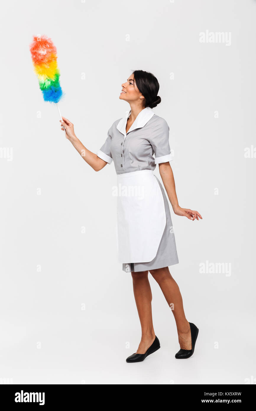 Volle Länge Foto von tidy weibliche Haushälterin in Uniform Streichbewegungen mit Staub sauberer, auf weißem Hintergrund Stockfoto