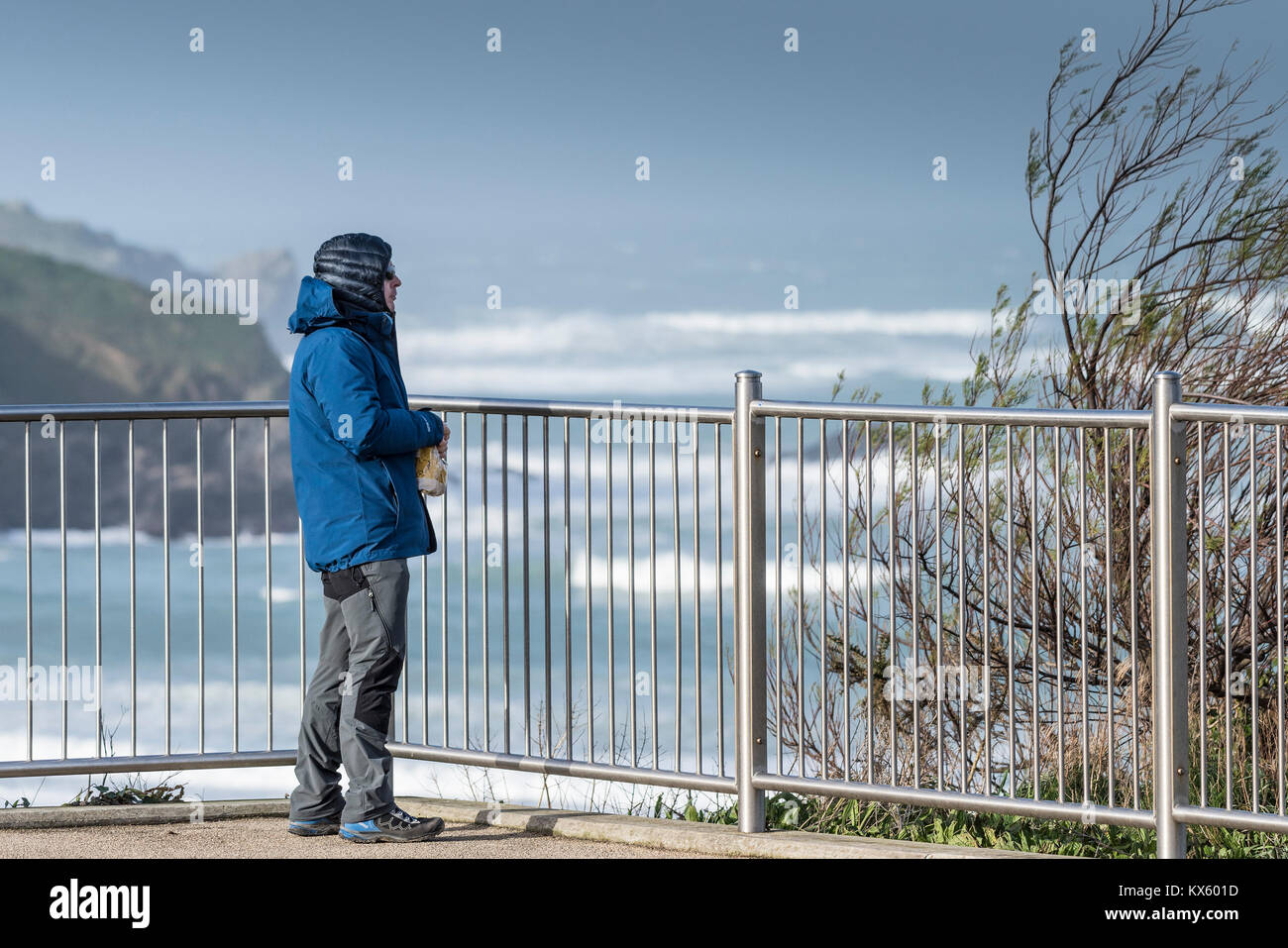 Ein Mann einen Snack essen und mit Blick auf das Meer, warme Kleidung tragen, gegen den kalten und windigen Wetter Stockfoto