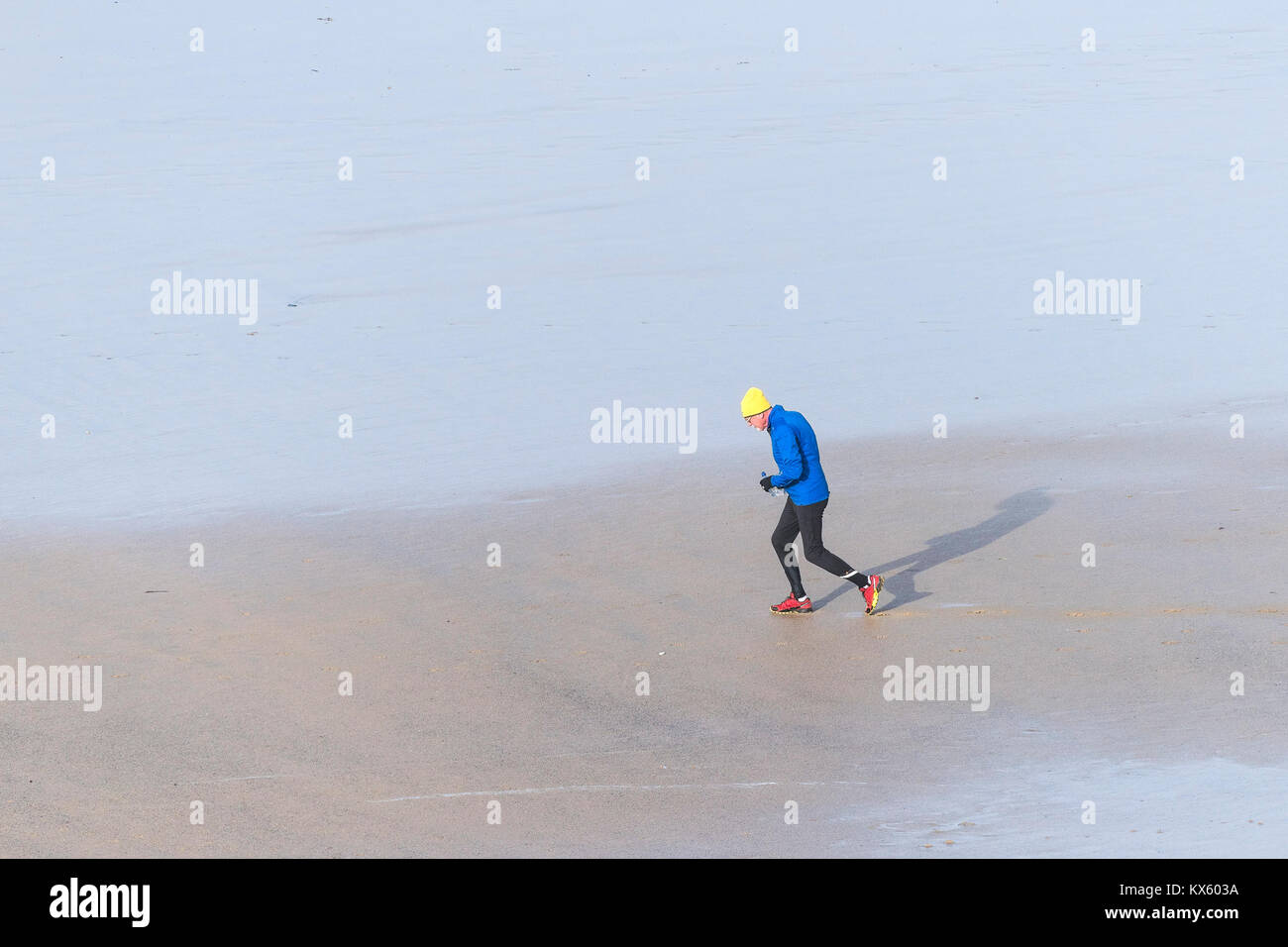 Ein reifer Mann tragen bunte Kleidung jogging über einen Strand bei Ebbe. Stockfoto