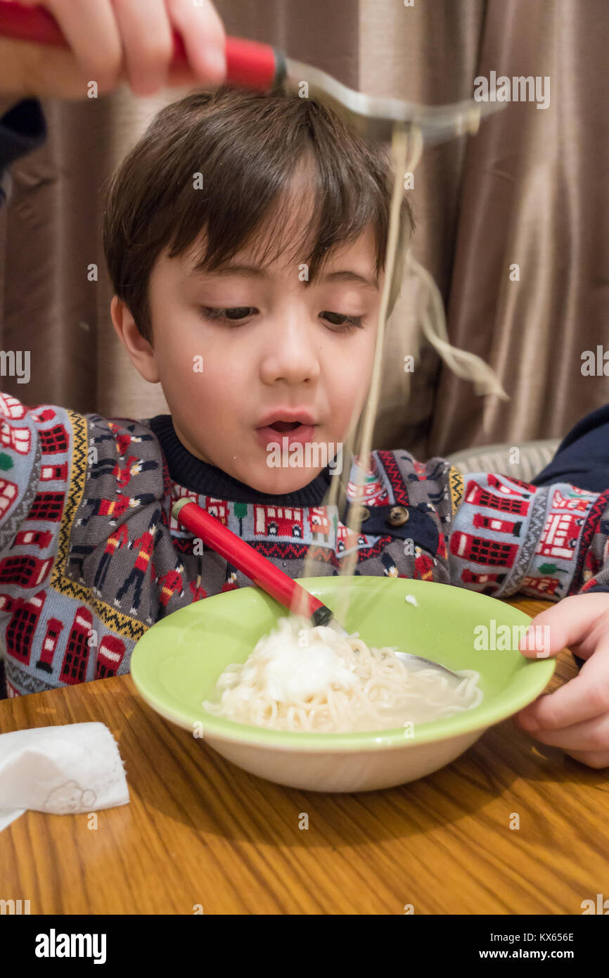 Ein kleiner Junge sitzt am Esstisch und isst eine Schüssel instant 'Soupy Nudeln. Stockfoto