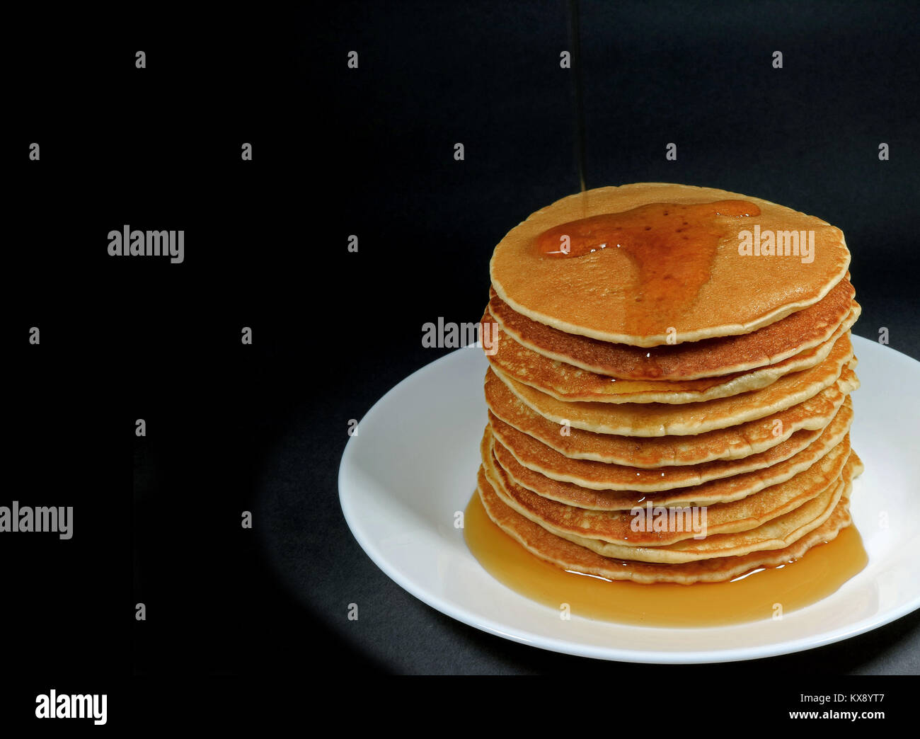 Stapel von Frische, hausgemachte Pfannkuchen mit Ahornsirup serviert auf weiße Platte, schwarzer Hintergrund mit Platz für Text oder Design Stockfoto