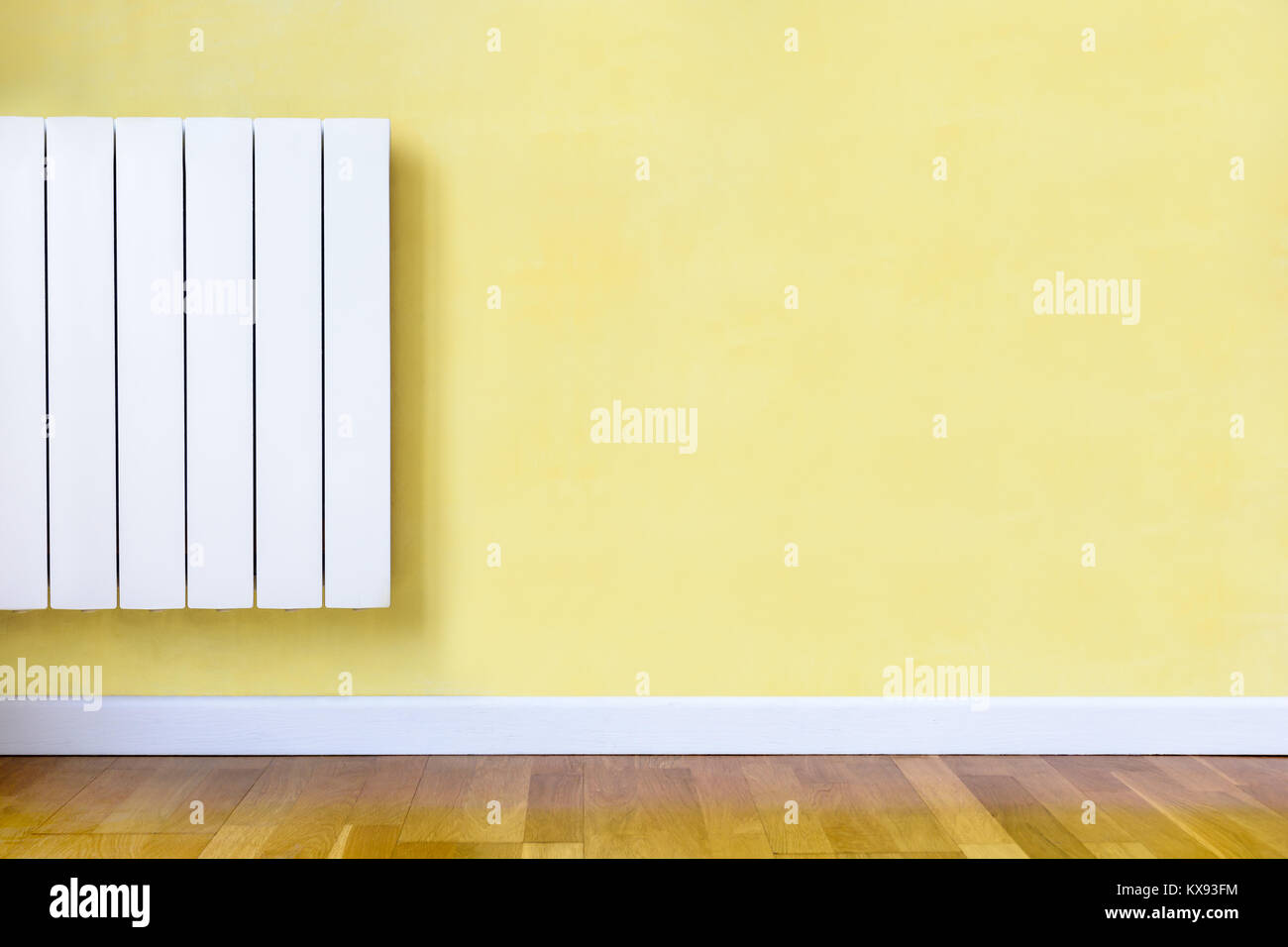 Modernes weißes elektrische Heizung mit Thermostat elektronisch in einem Zimmer mit gelber Wand montiert, Holzböden und weißen Baseboard. Stockfoto