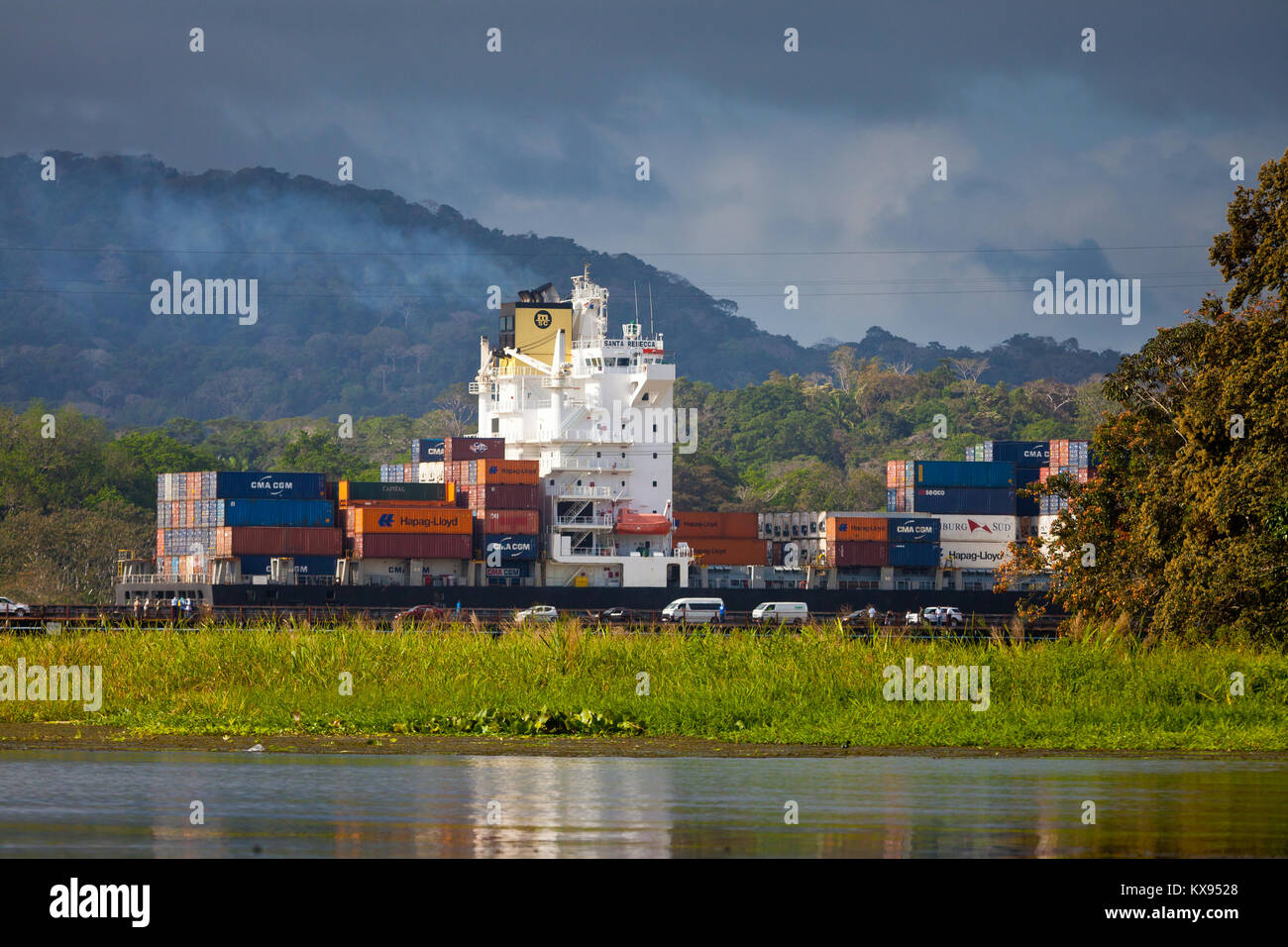 Container schiff durch den Panamakanal bei Gamboa, Republik Panama. Im Vordergrund Autos warten auf grünes Licht, die Brücke zu überqueren. Stockfoto