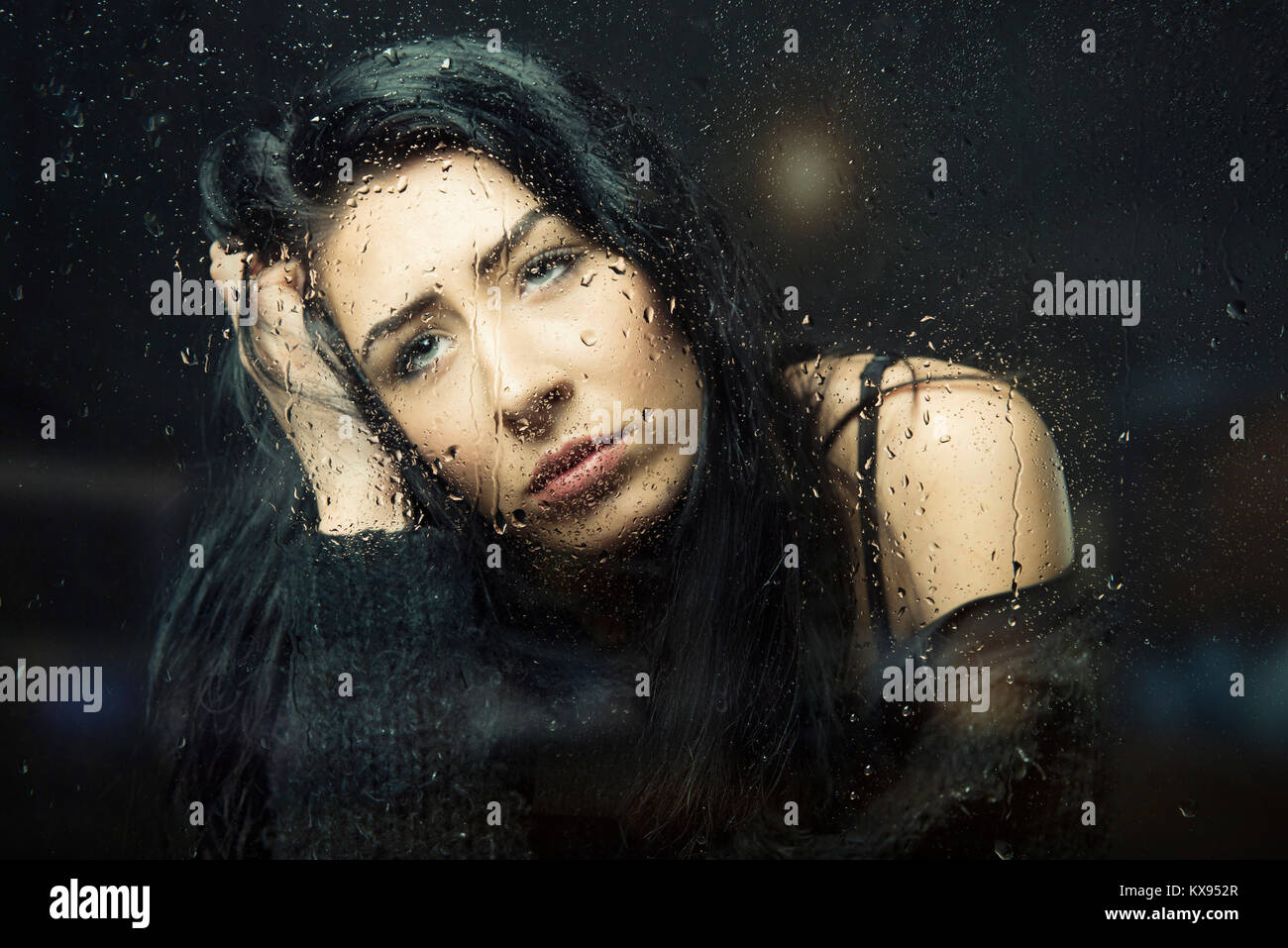 Frau traurig, deprimiert, die Hand auf den Kopf am verregneten Fenster closeup filmischen Porträt sitzen Stockfoto