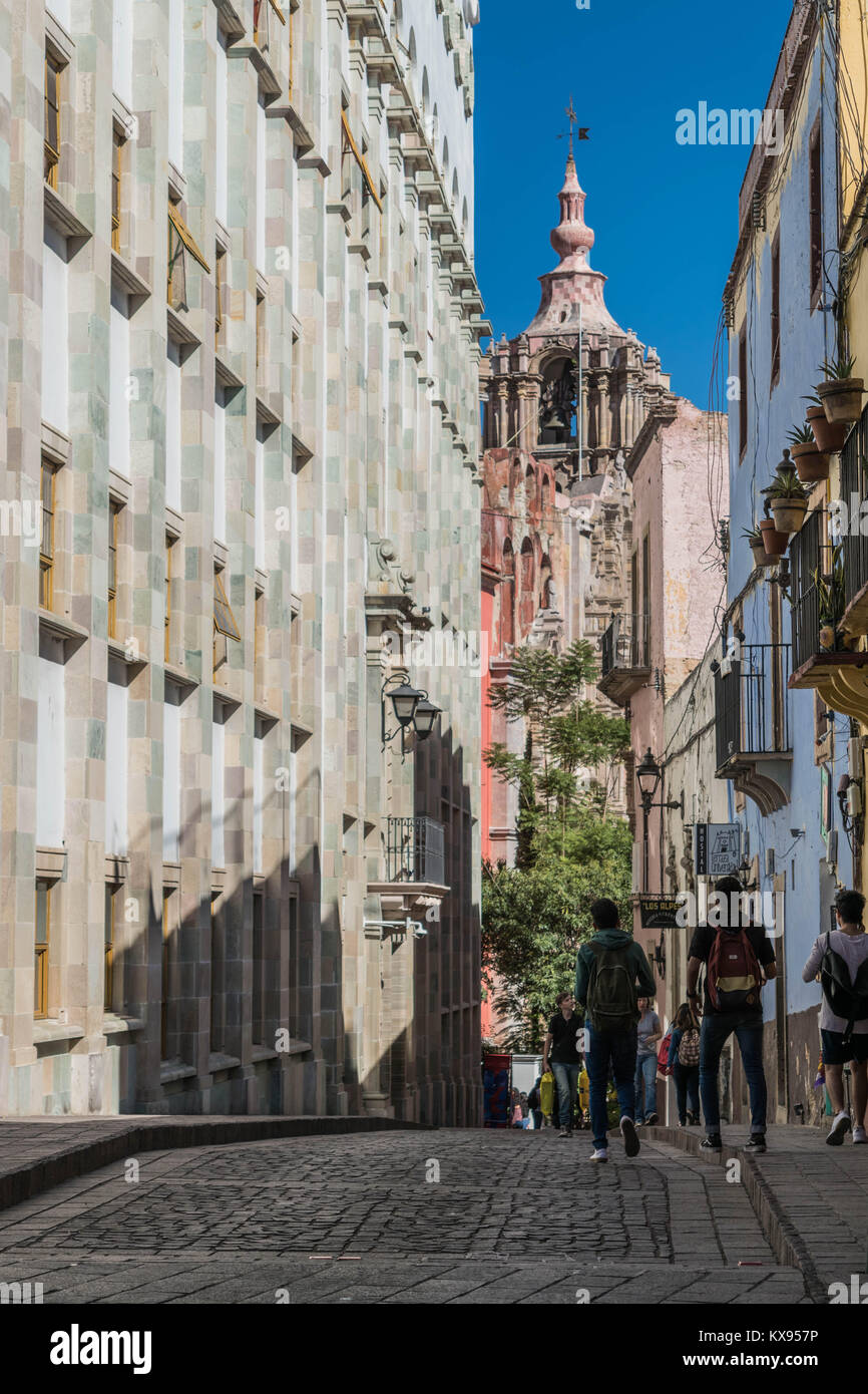 Street Scene mit Fußgängern, alte Gebäude, Kopfsteinpflaster, eine alte Kirche, Glockenturm und einem klaren blauen Himmel, in Guanajuato, Mexiko Stockfoto