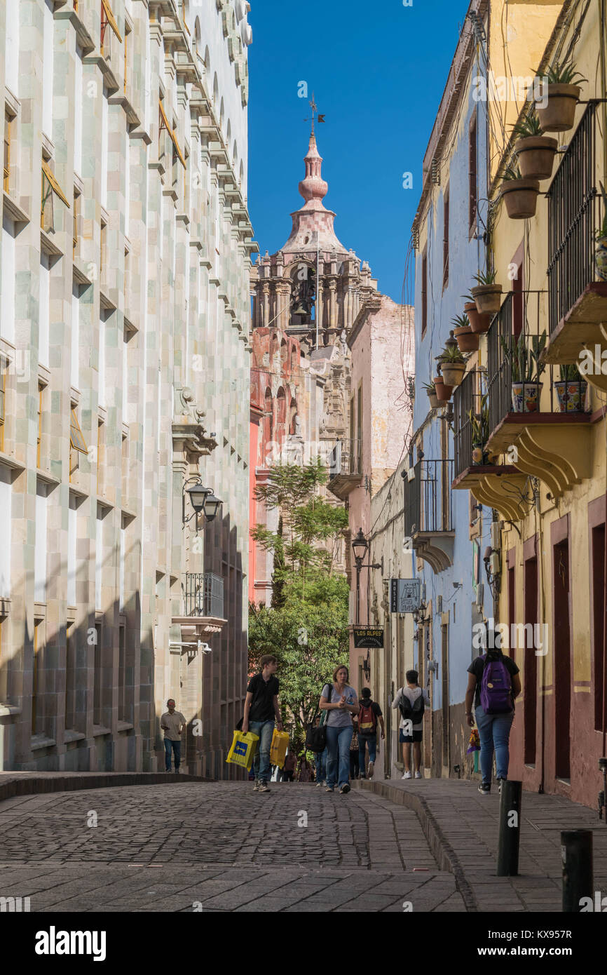 Street Scene mit Fußgängern, alte Gebäude, Kopfsteinpflaster, eine alte Kirche, Glockenturm und einem klaren blauen Himmel, in Guanajuato, Mexiko Stockfoto