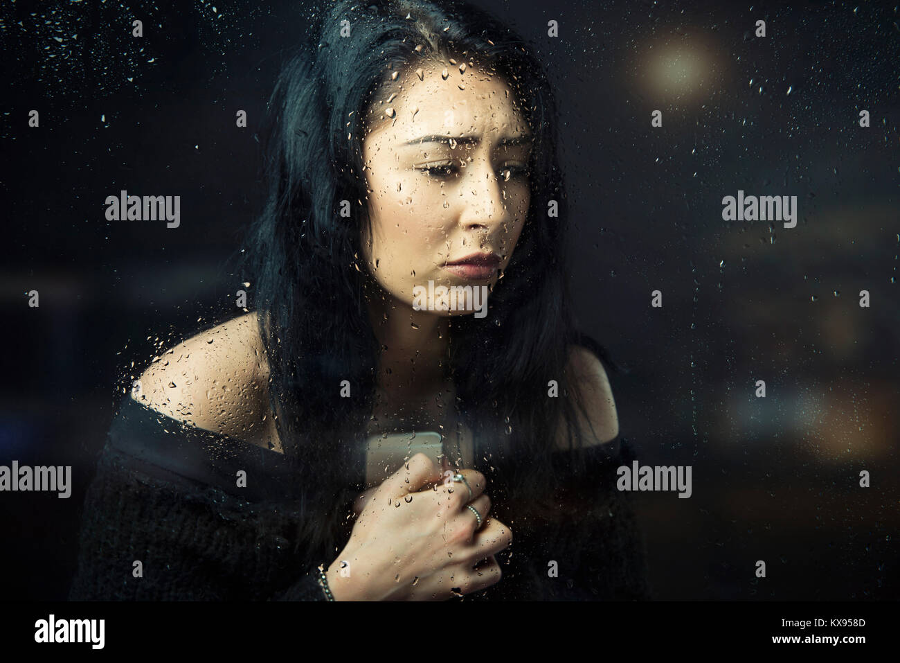 Traurige junge Frau umklammert Handy Seite Profil weinen suchen verzweifelt sitzen an regnerischen Fenster filmische Nahaufnahme portrait gedrückt Stockfoto