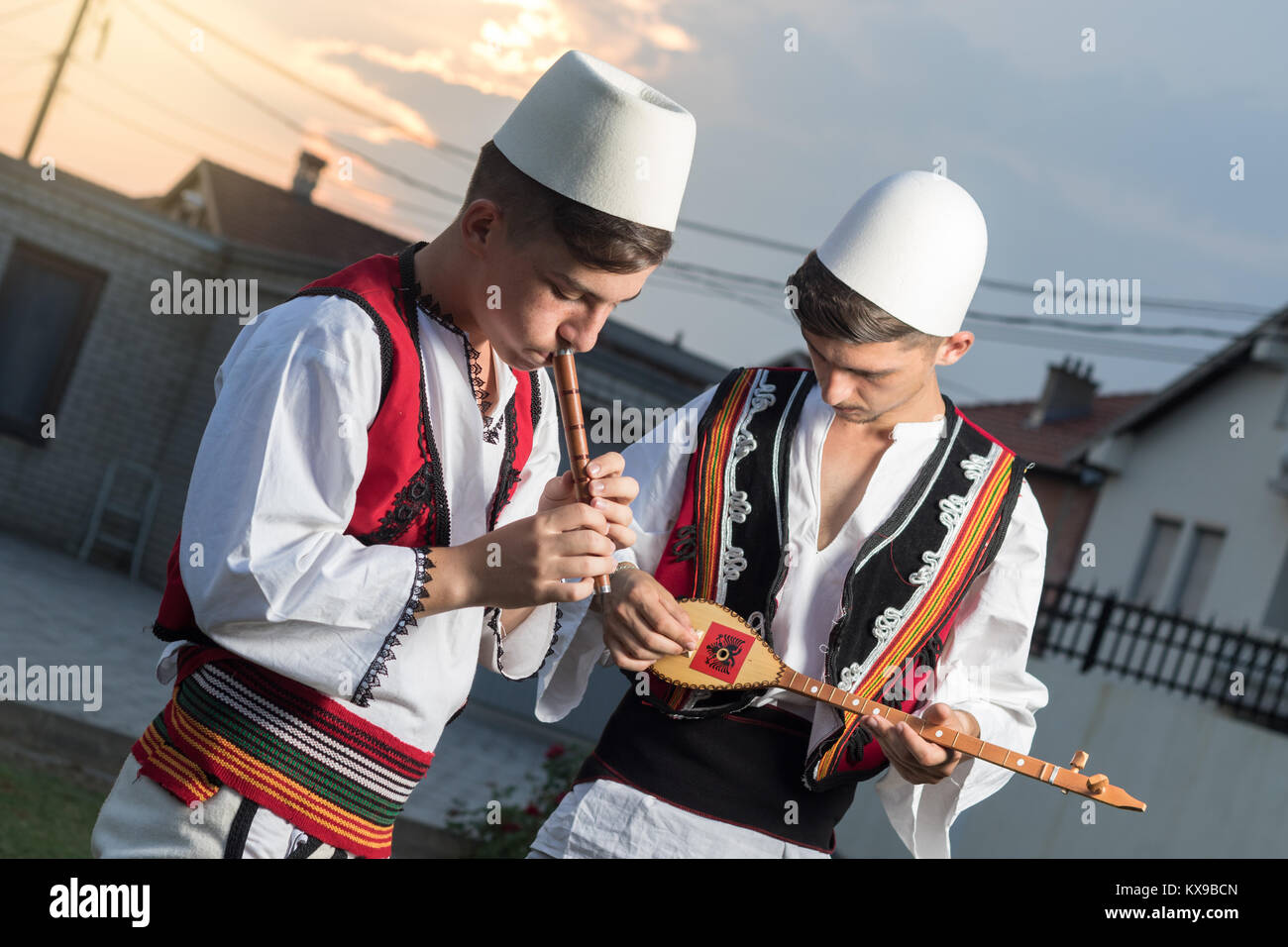 Jugendlich Jungen in der traditionellen albanischen Kostüm spielen Musik mit Flöte und String Instrument in der Abendsonne Stockfoto