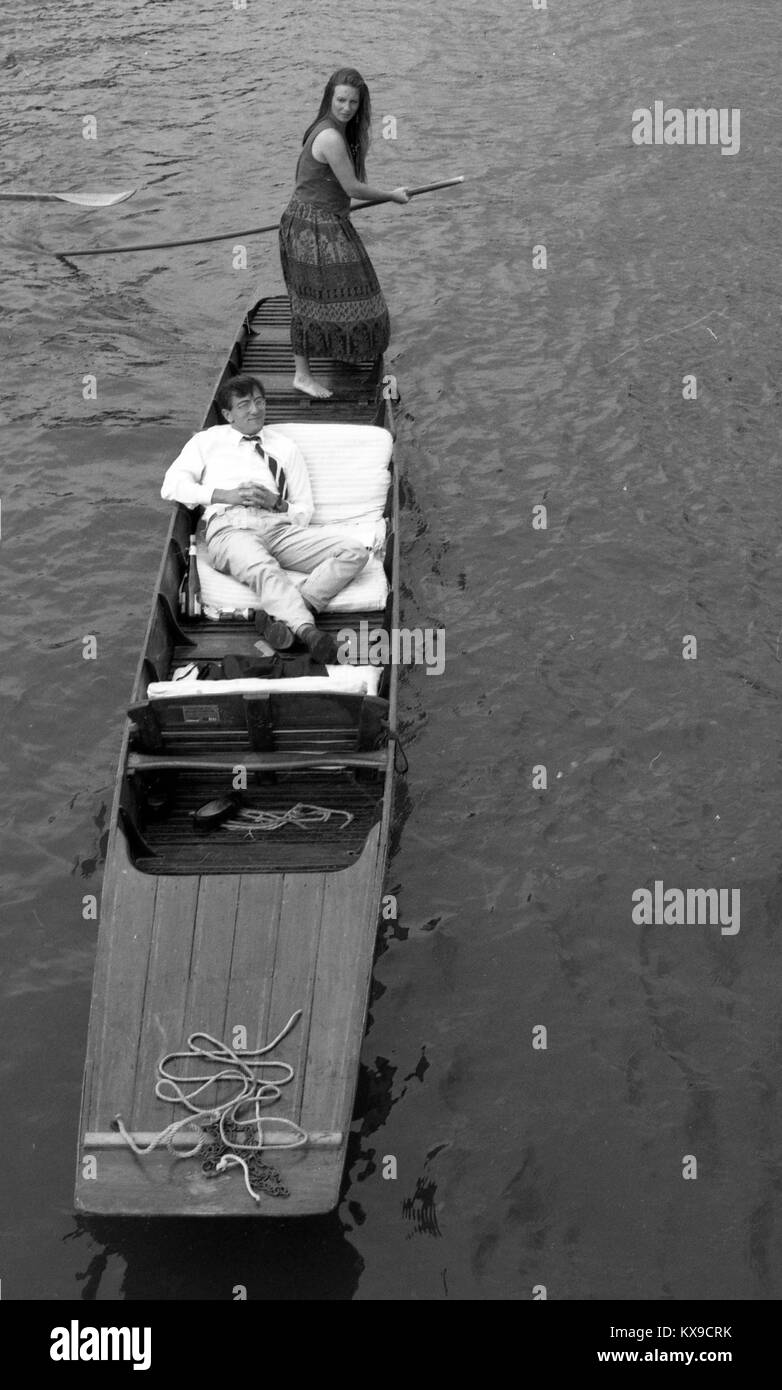 Juli 1990, Henley on Thames, Oxfordshire, England. Henley Royal Regatta Szene auf der Themse. Ein Mann entspannt, während eine Frau stocherkähne am Henley Foto von Tony Henshaw Stockfoto