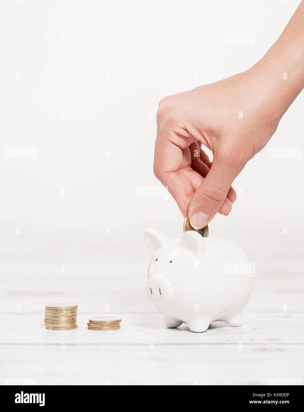 Piggy Bank und Münze in weibliche Hände über dem weißen Holz- Hintergrund Stockfoto