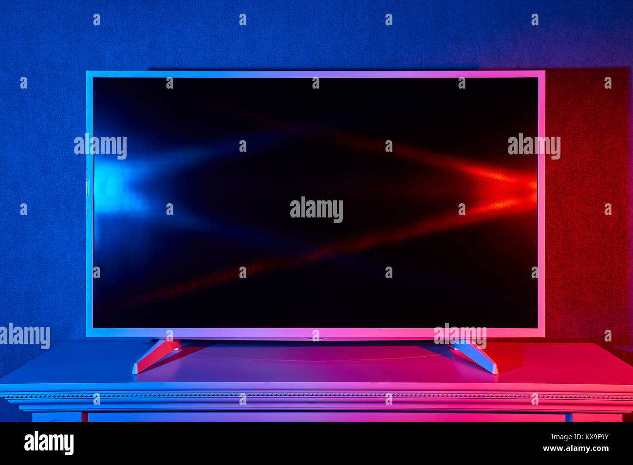 Eine moderne flache LED-TV auf einem Ständer leuchtet rot und blau Stockfoto