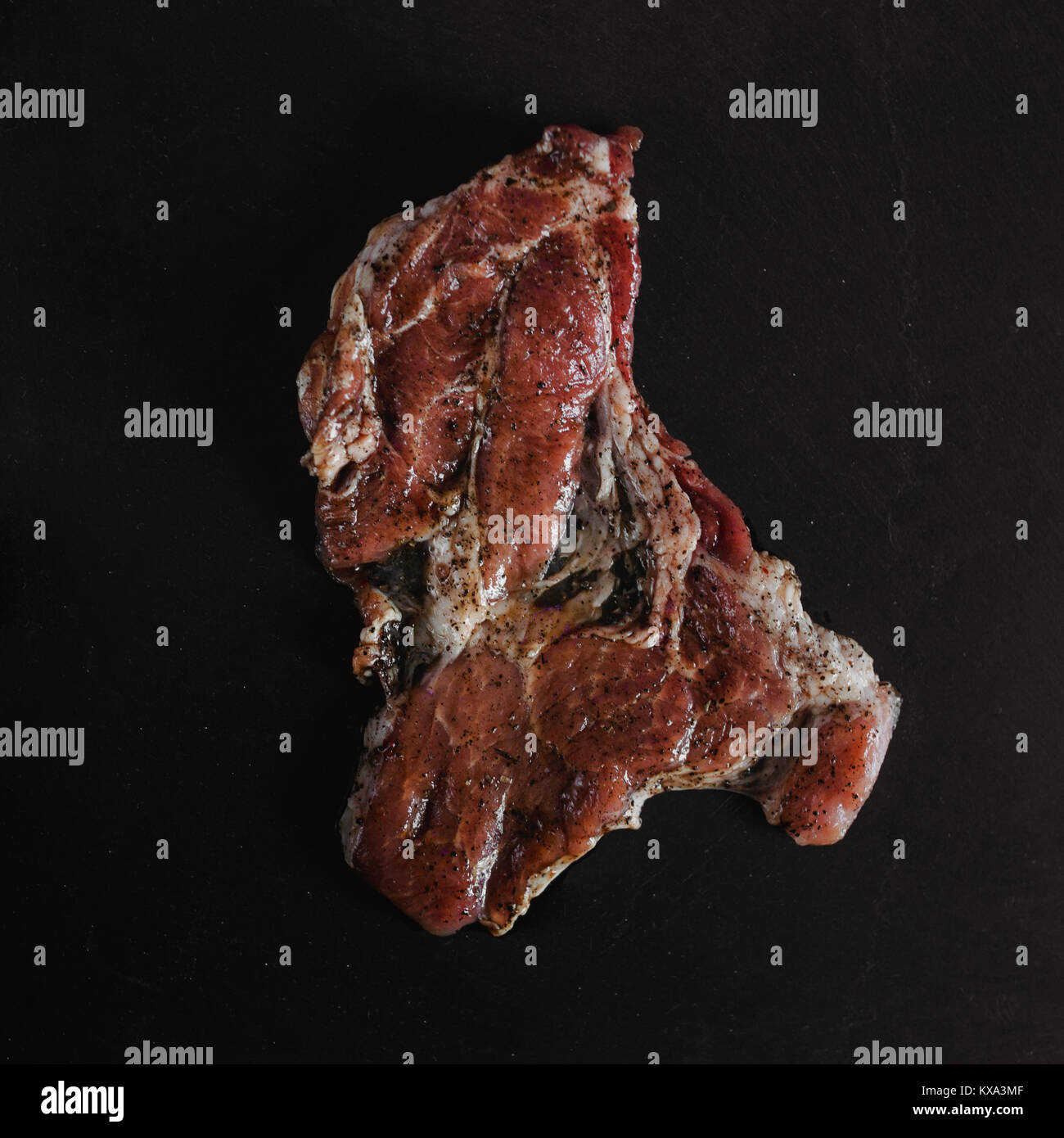 Essen Foto im rustikalen Stil. Mariniertes Fleisch. Schweinesteak auf dunklen schwarzen Hintergrund von Schiefer. Ansicht von oben. Flach. Stockfoto