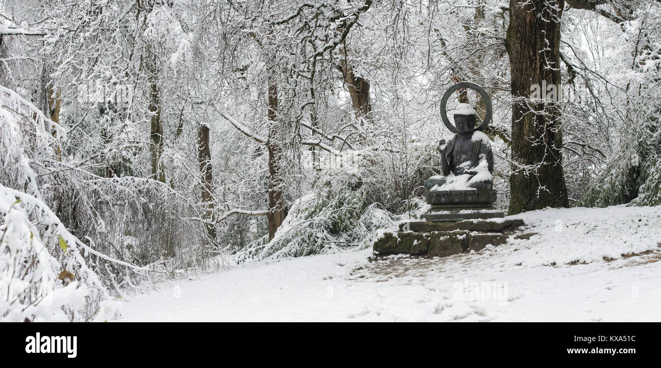 Buddha Statue und Winter Bäume im Schnee im Dezember bei Batsford Arboretum, Cotswolds, Moreton-in-Marsh, Gloucestershire, England. Panoramablick Stockfoto