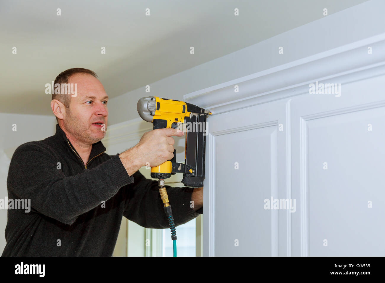 Handwerker arbeiten mit Brad Nagel Druckluftpistole zu Stuckelemente auf weißen Küche Wandschränke Verkleidung, mit der alle Power Tools Stockfoto