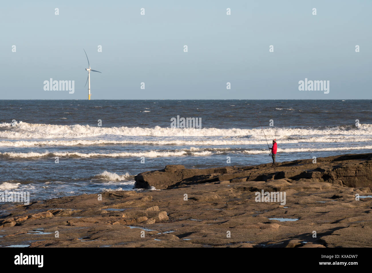 Ein angler angeln mit Stab und Linie nördlich von Seaton Sluice, mit einer Windkraftanlage im Hintergrund, Northumberland, England, Großbritannien Stockfoto