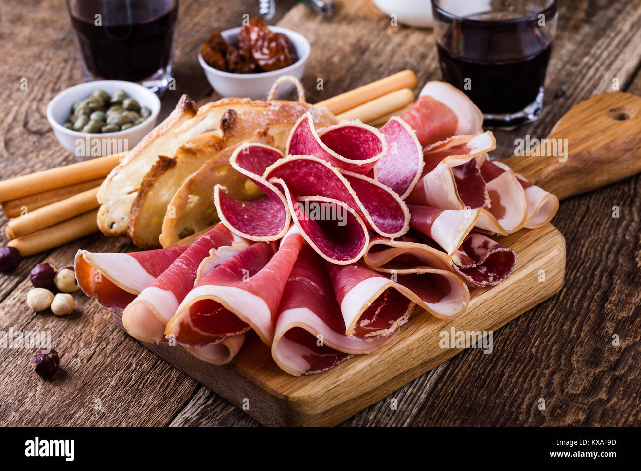 Geräuchertes Fleisch Antipasti Platte mit Toast, Brot Sticks und Rotwein auf dem Holztisch serviert. Italienisches Essen, Prosciutto, Salami, getrocknete Tomaten Stockfoto
