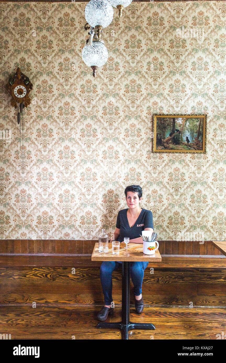 Der Küchenchef Eigentümer von Karchka Restaurant in Portland sitzt an einem kleinen Tisch mit einer alten europäischen Stil Tapete drucken hinter ihr. Stockfoto