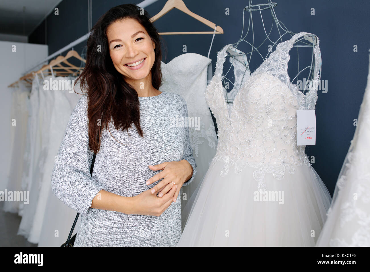 Attraktive junge Braut lächelnd, während sie Hochzeit Kleid in Bridal Boutique. Lächelnd asiatische Frau Einkaufen für Hochzeit Ausstattung in Braut Kleidung sto Stockfoto