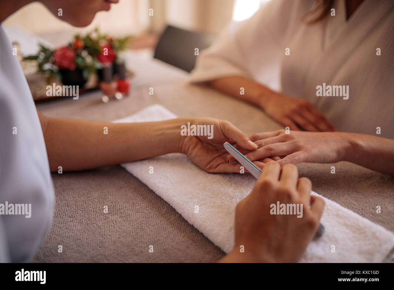 Hände von qualifizierten Maniküre Feilen der Nägel Client von einer Frau mit einem weißen Puffer im Nagelstudio. Fokus auf Hände Maniküre Formen der Nägel der weiblichen Stockfoto